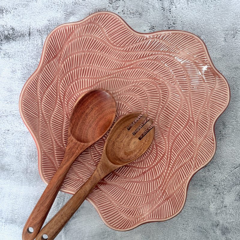 Pink scalloped plate with carved lines and wooden servers.