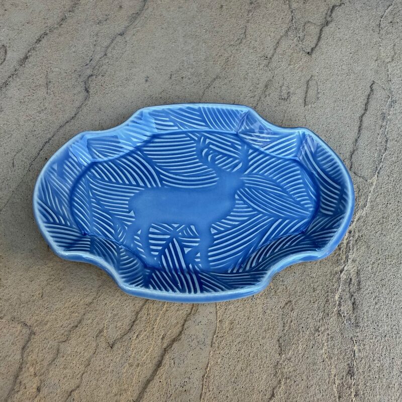Blue oval ceramic dish with carved deer silhouette and leaf pattern displayed on a neutral background