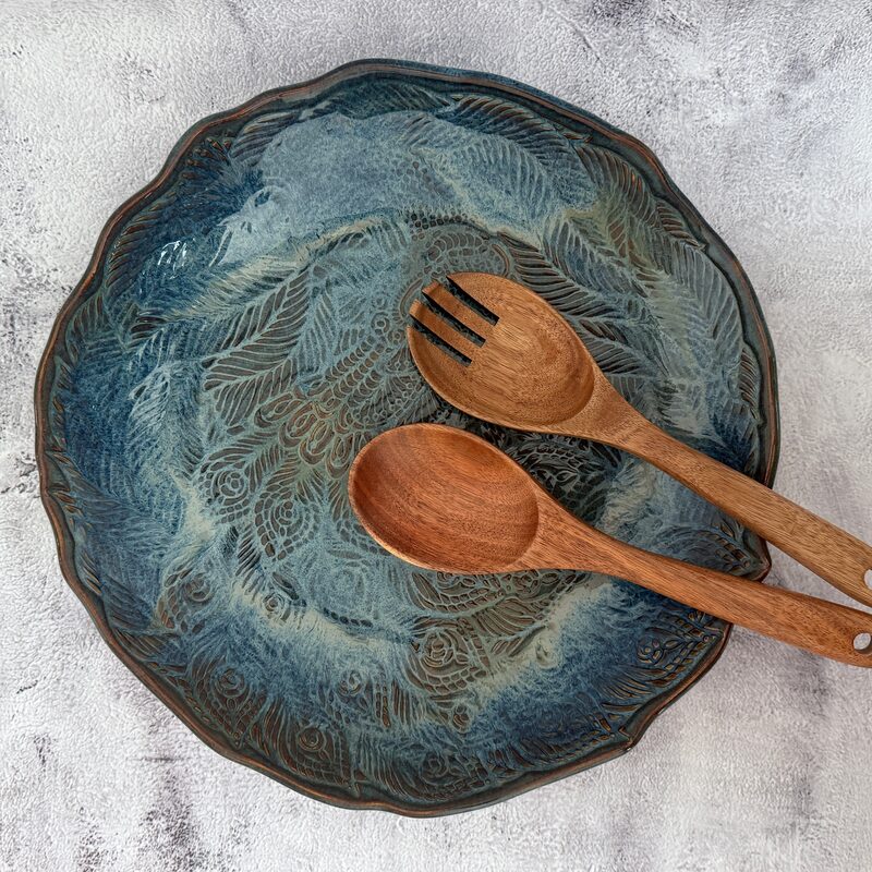 Large blue ceramic serving bowl with carved feather pattern styled with wooden salad servers