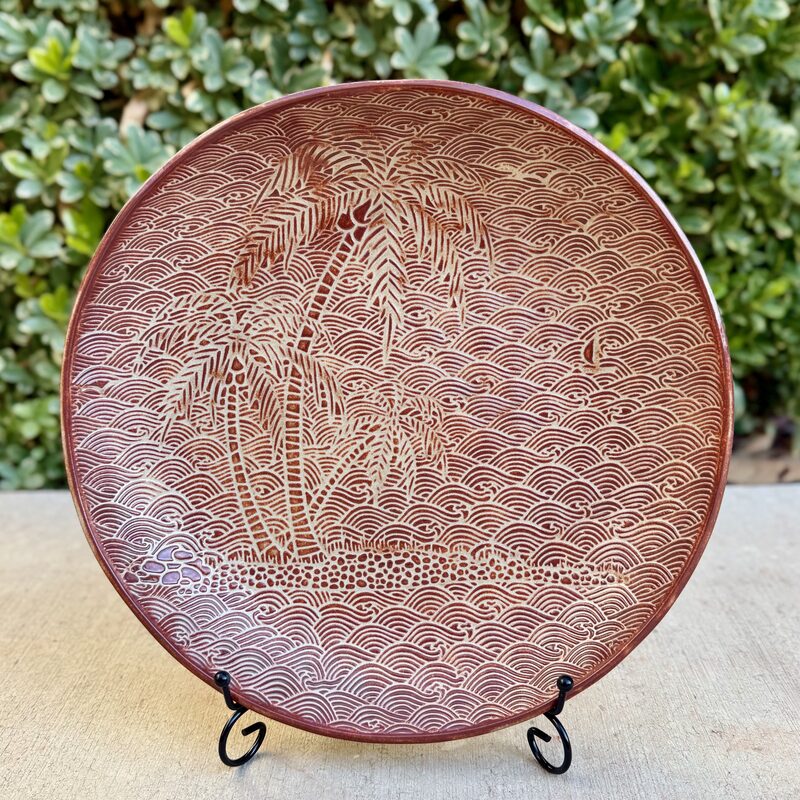 Large round brown ceramic platter with palm tree pattern presented on a display stand